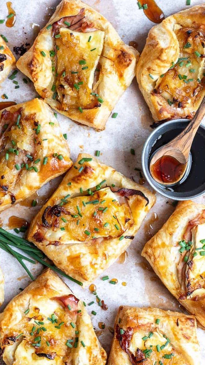 Ham and brie puff pastry appetizers topped with chives on a baking sheet.