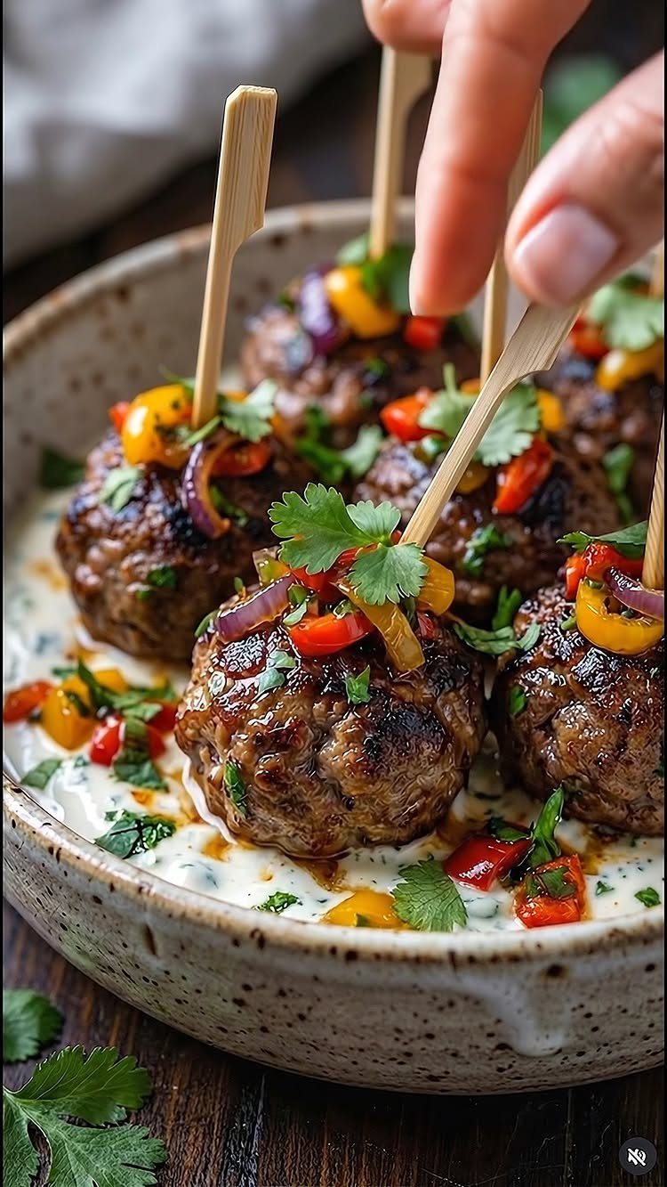 Meatballs with diced peppers and cilantro on skewers in a creamy sauce bowl