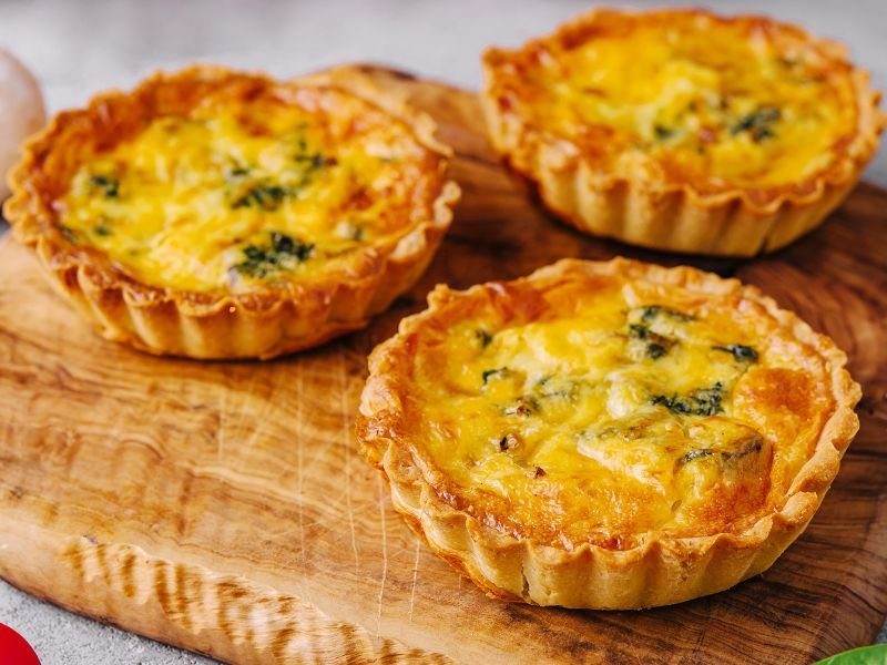 Three mini broccoli quiches with golden crusts on a wooden board.