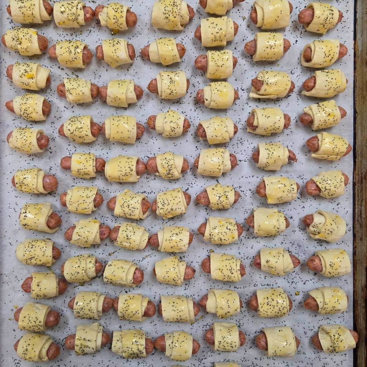 Small sausages wrapped in pastry dough on a baking sheet with black pepper.
