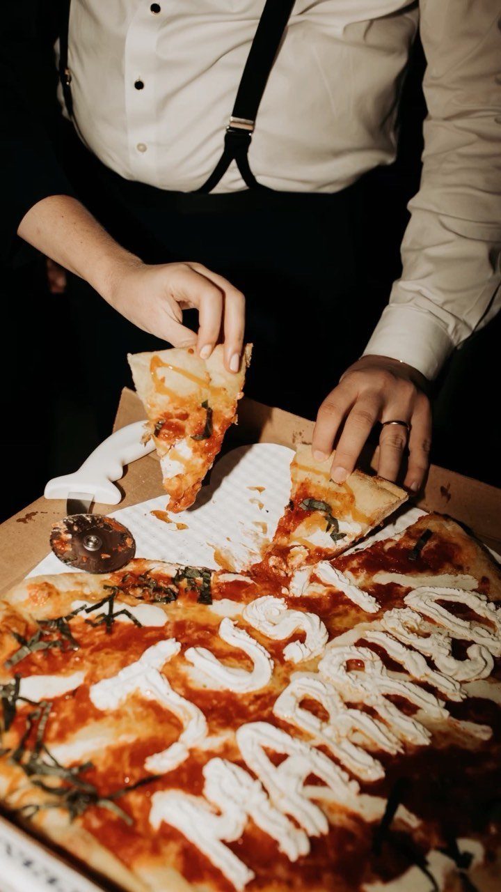 Pizza with Just Married written in cheese, held by a person in suspenders.