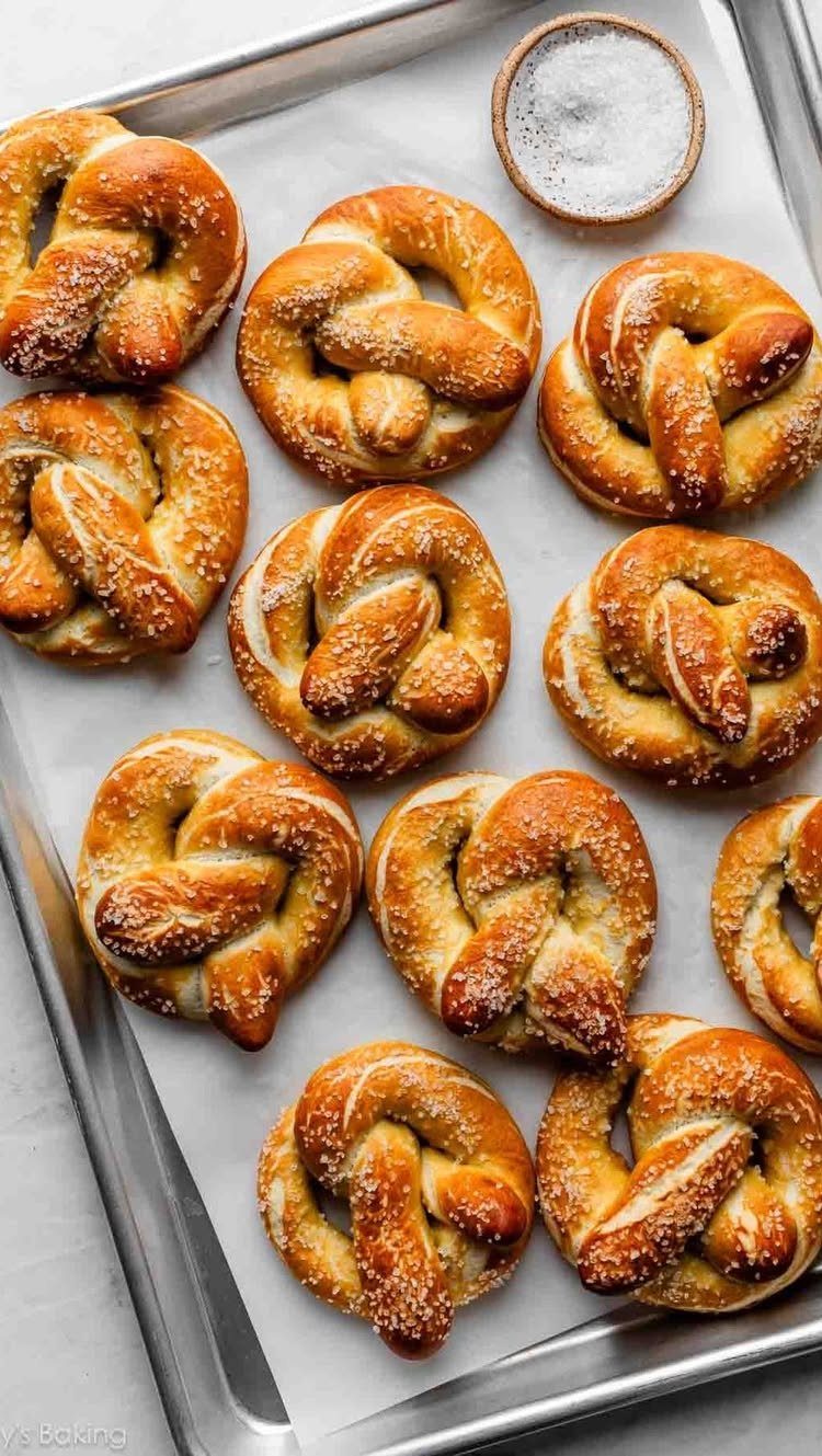 Golden-brown salted soft pretzels on a baking sheet with a bowl of salt.
