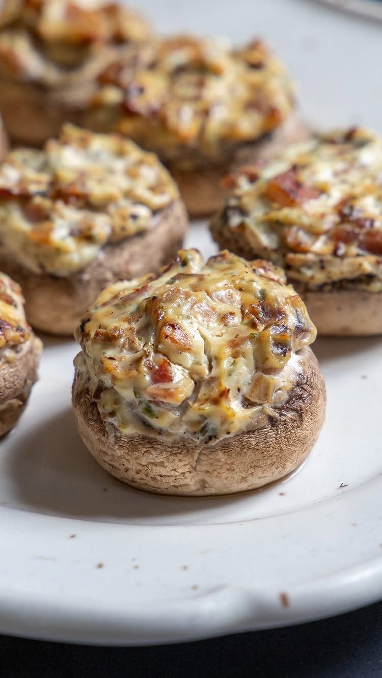 Stuffed mushroom caps with golden brown creamy filling on a white platter