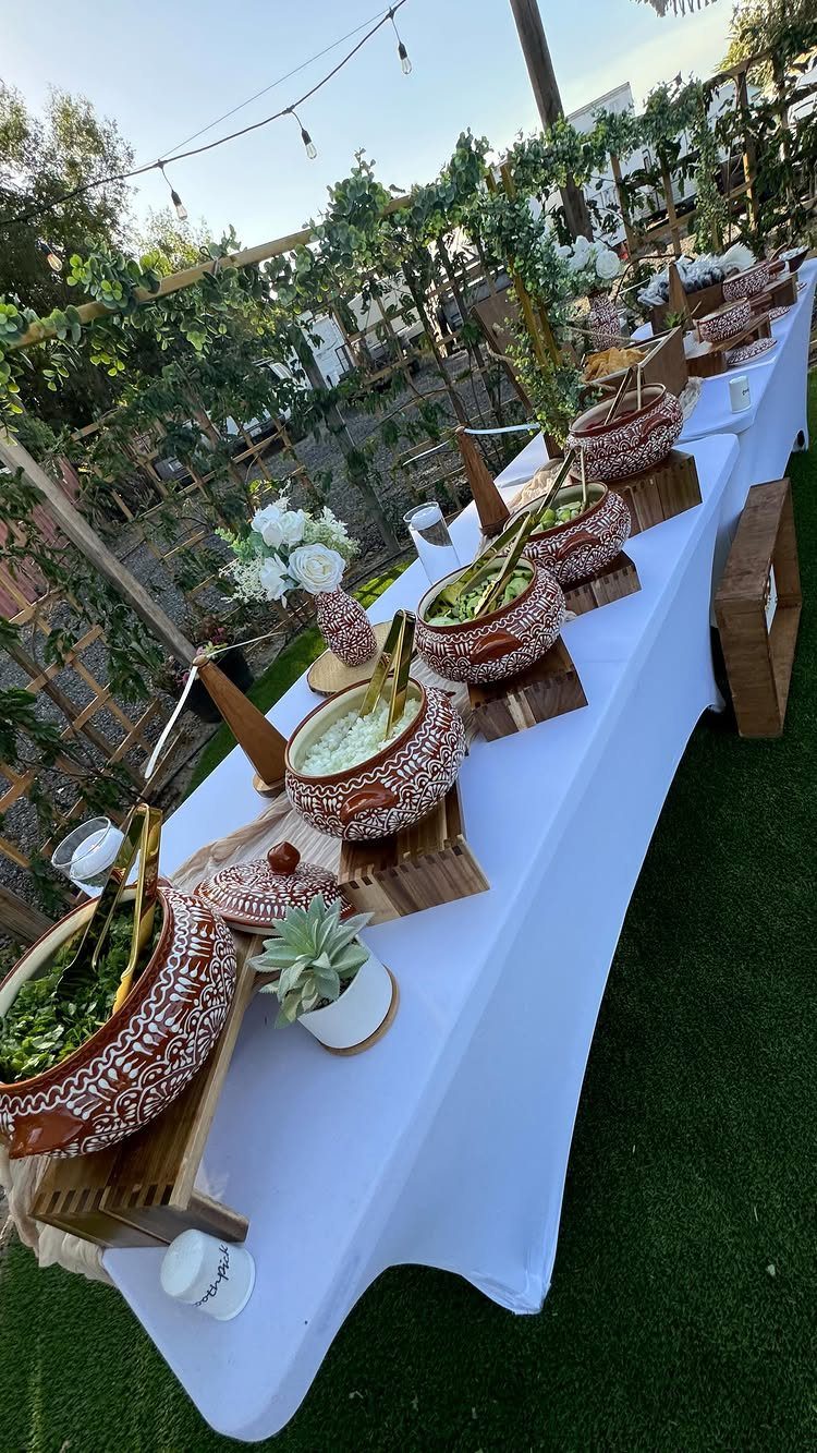 Taco bar setup with patterned ceramic pots of toppings on a white tablecloth.