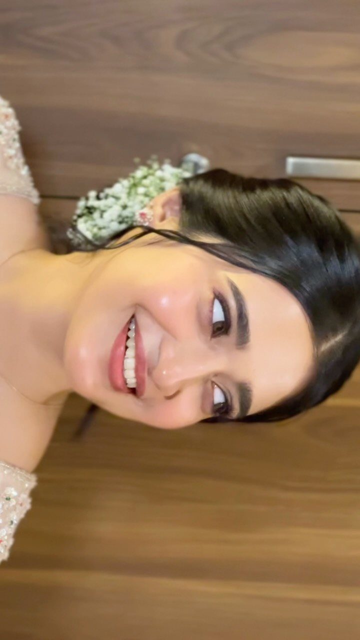 Woman with soft defined makeup, dark hair, and white flowers in her hair.