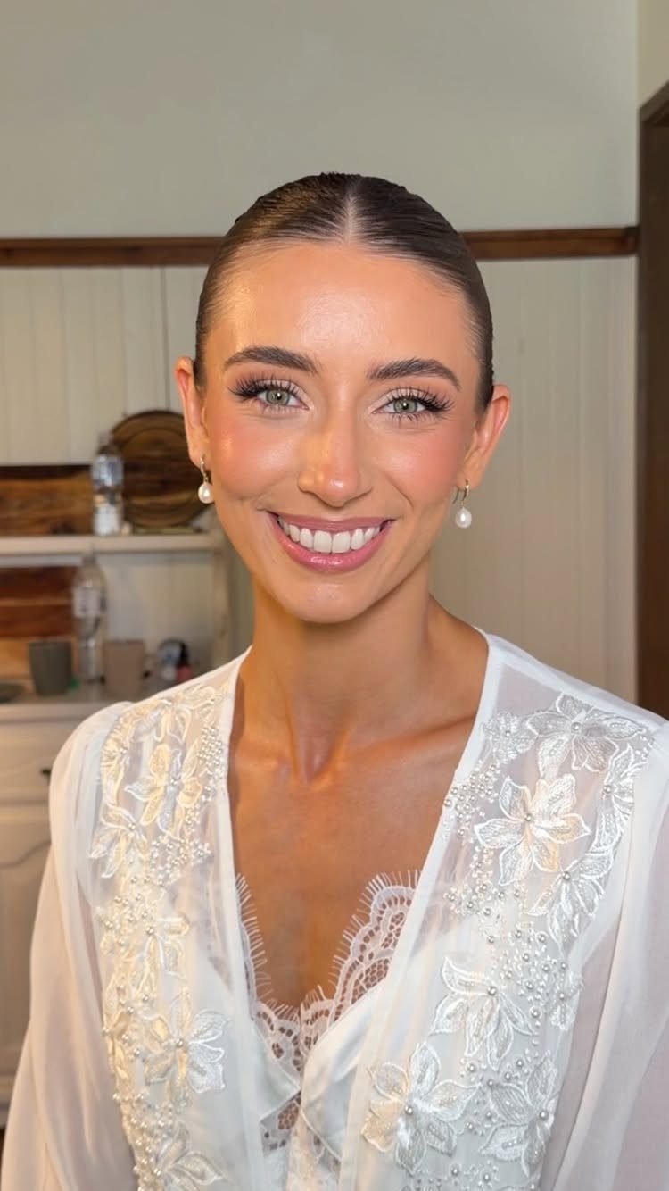 Woman in white lace bridal robe with soft, natural wedding makeup and pearl earrings.