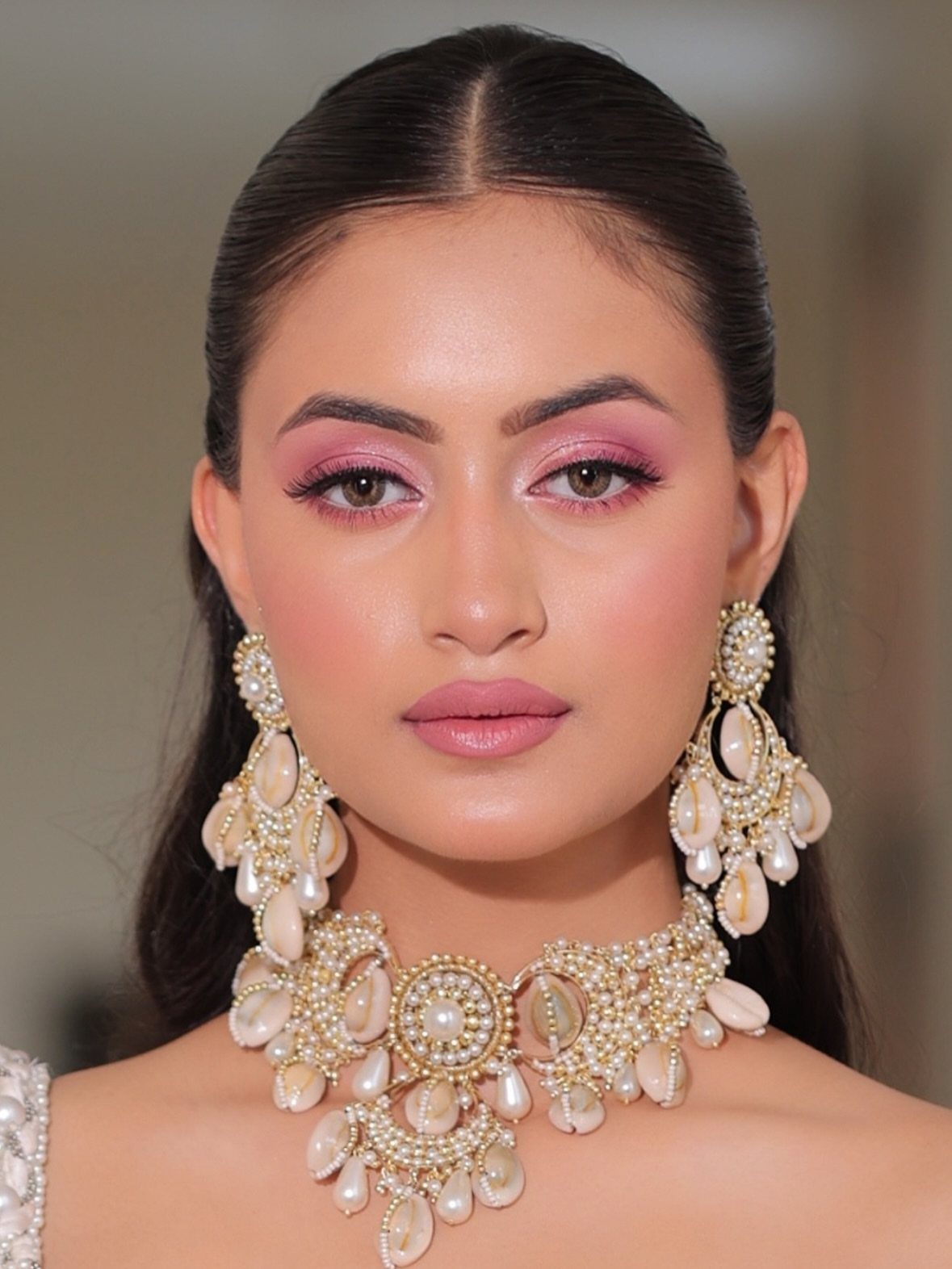 Woman with pink eyeshadow and pearl jewelry posing for a bridal makeup portrait.