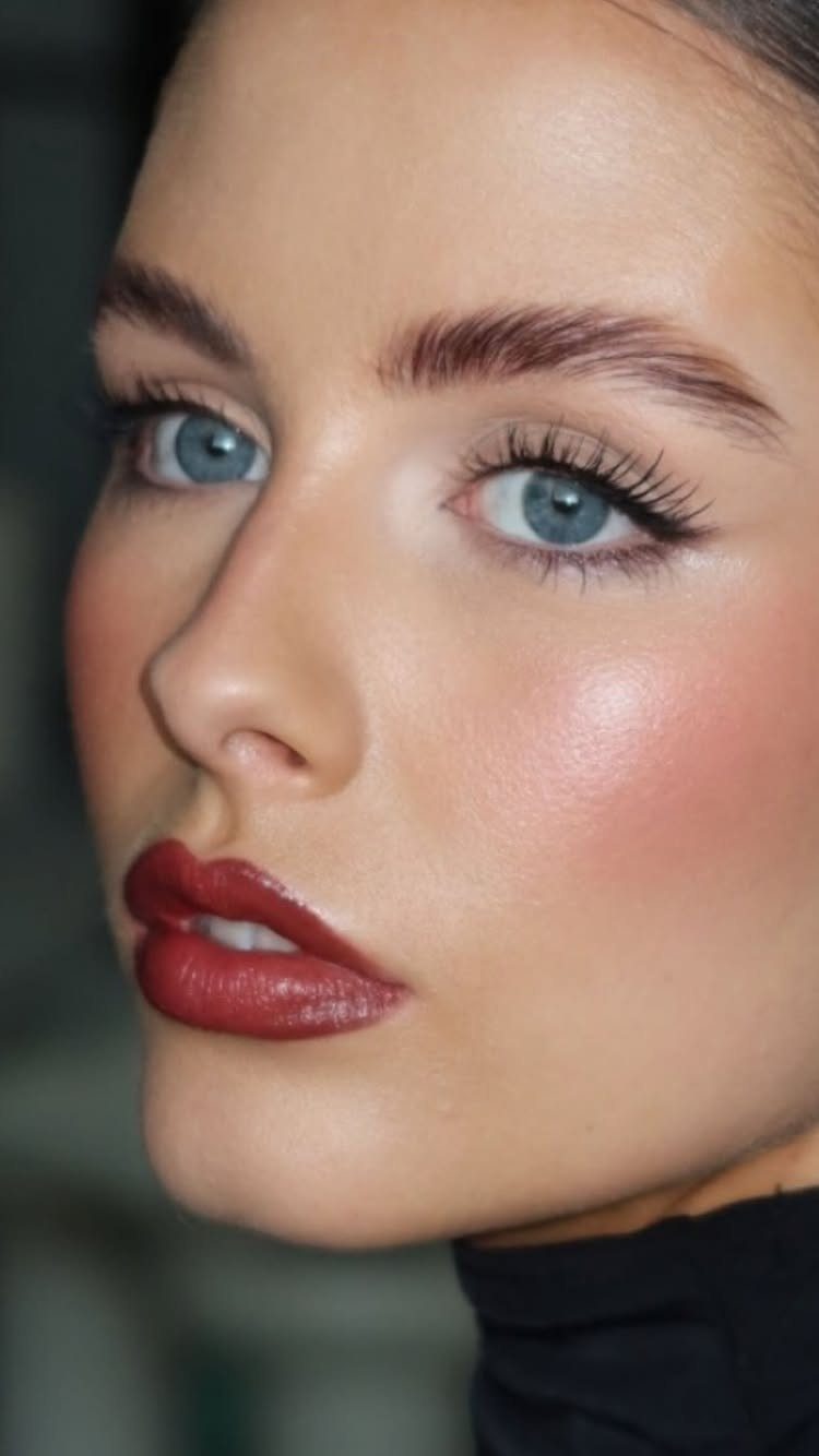 Woman with glowing skin, blue eyes, and bold red lipstick in close-up.
