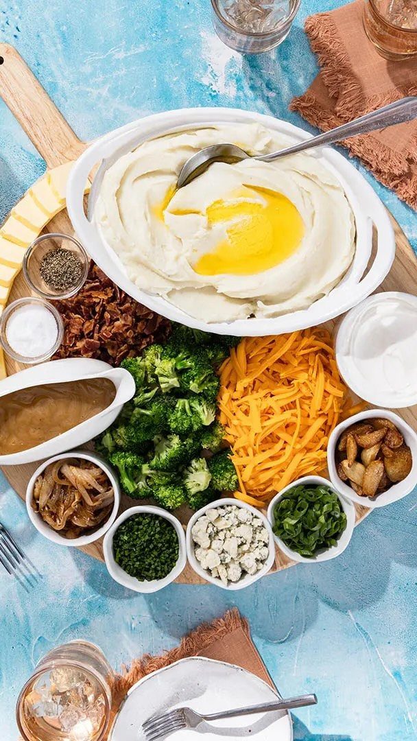 Mashed potato bar with various toppings like cheese and broccoli on a wooden board.