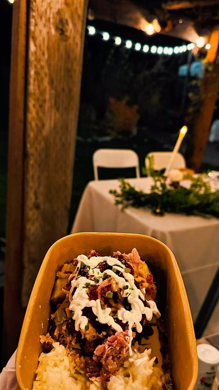 Loaded potato with meat, cream, and chives in a cardboard container outdoors.