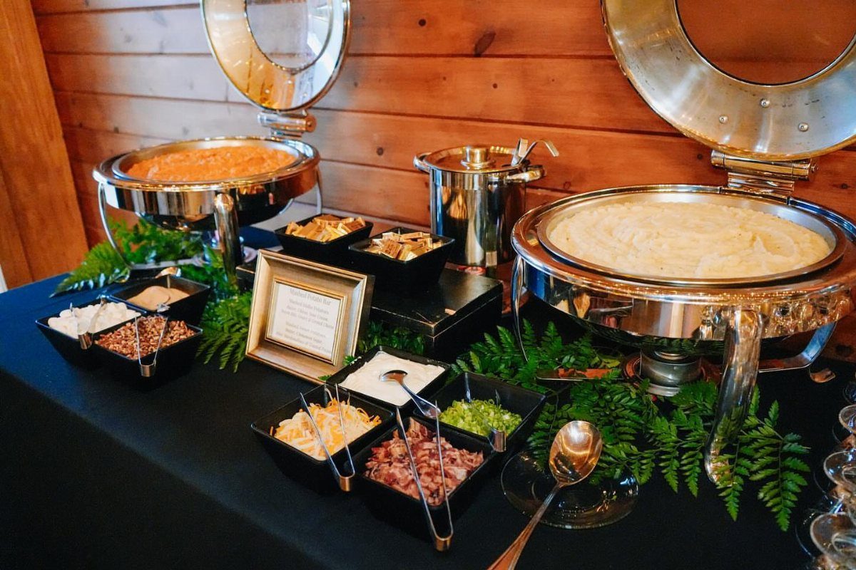 Buffet table with silver chafing dishes of potatoes and various topping bowls.