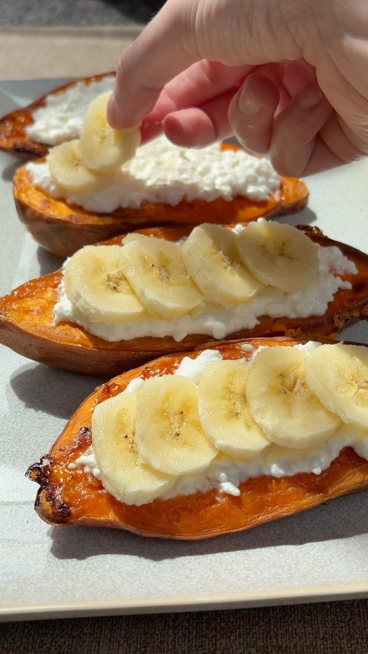 Roasted sweet potatoes topped with white cream and sliced bananas on a grey platter.