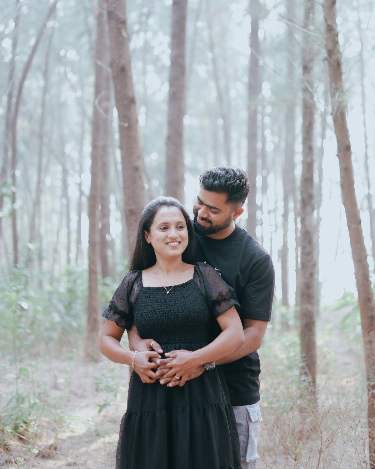 Couple embracing and smiling in a forest of tall, thin trees.