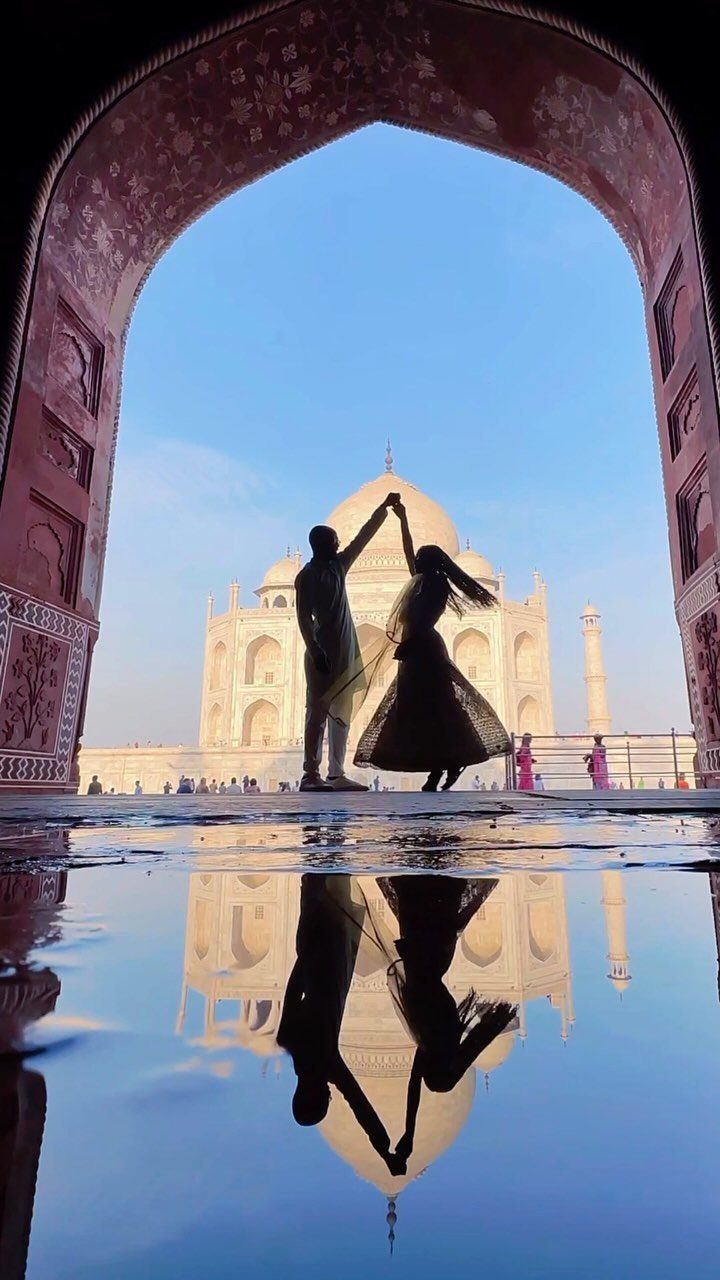 Couple dancing in silhouette before the Taj Mahal, reflected in a water puddle.
