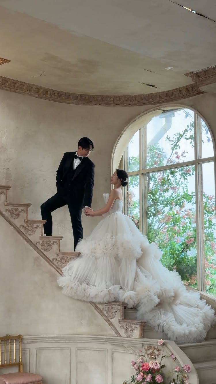 Couple in wedding attire posing on a grand staircase in a studio setting