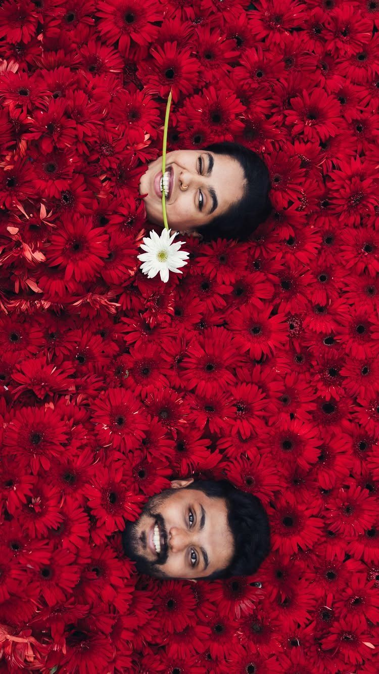 Couple smiling while lying in a bed of red daisies with one white flower