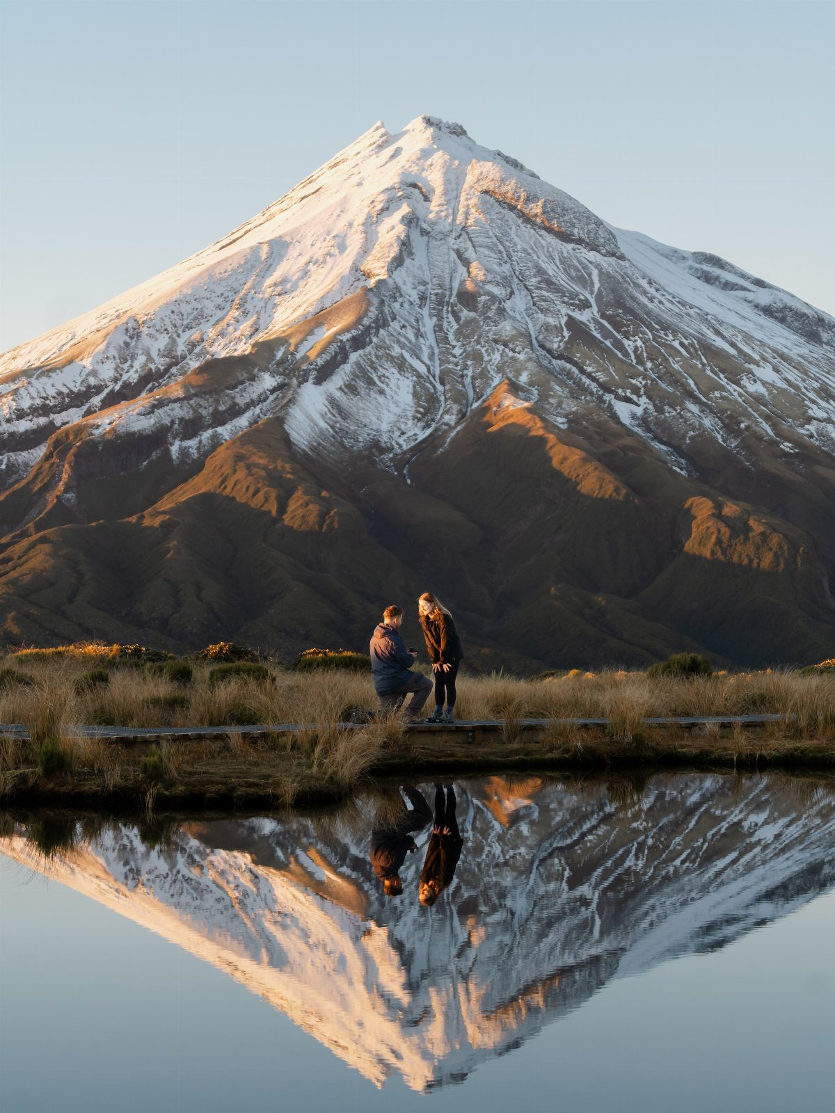 Couple proposing in front of a snow-capped mountain reflected in a still lake