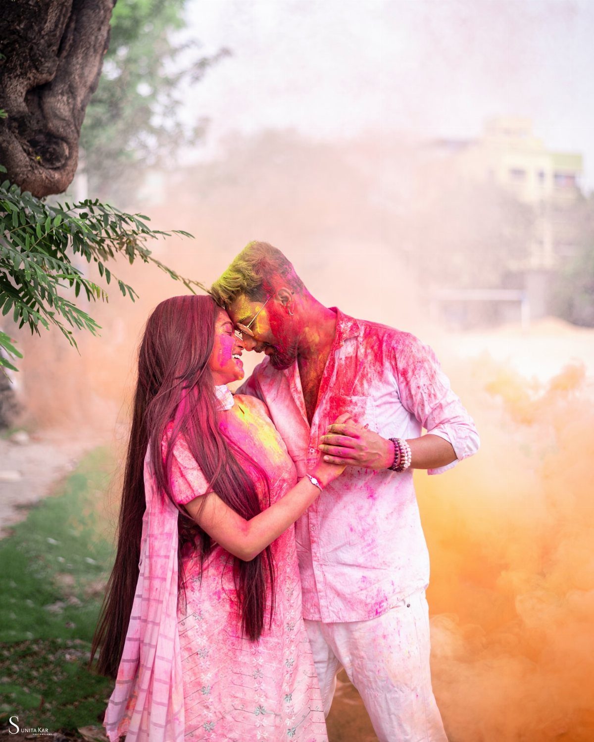 Couple in white clothes covered in colorful powders holding hands outdoors.