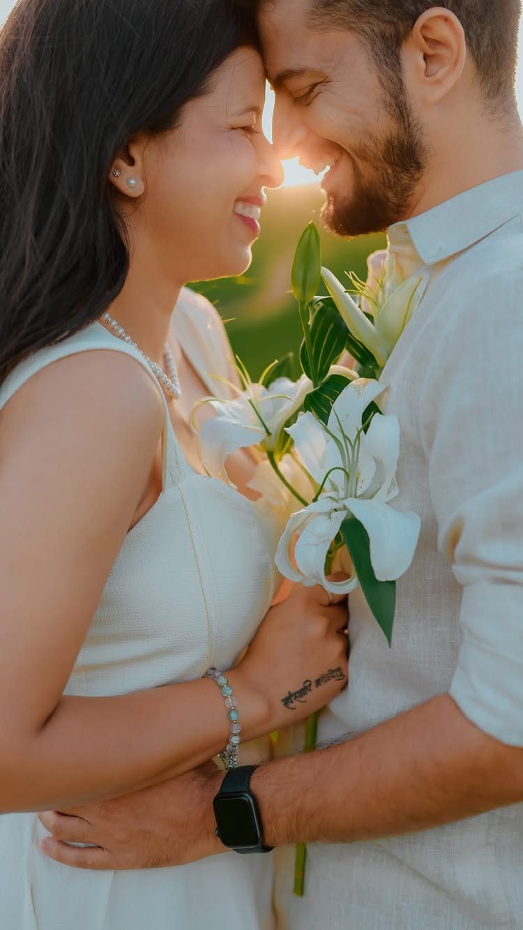 Smiling couple in white embracing outdoors with white lilies during golden hour