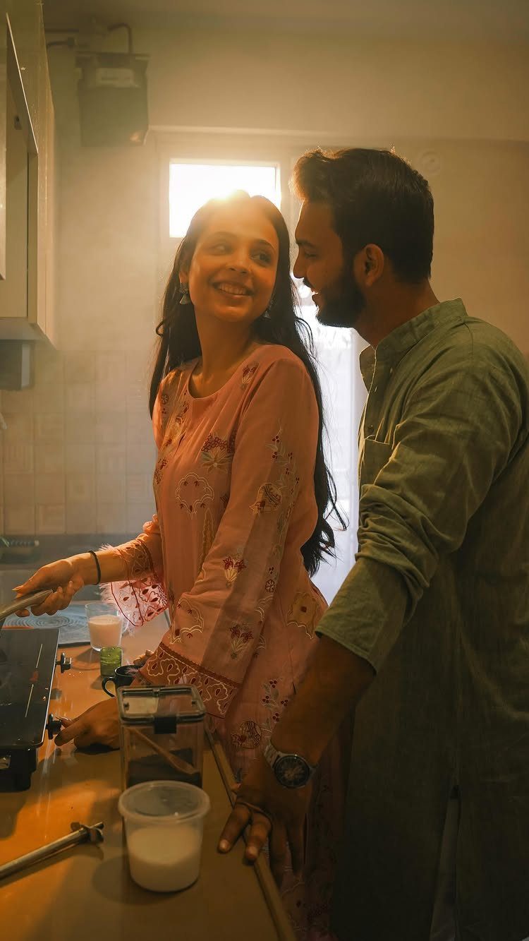 Couple smiling and cooking together in a kitchen with warm backlight.