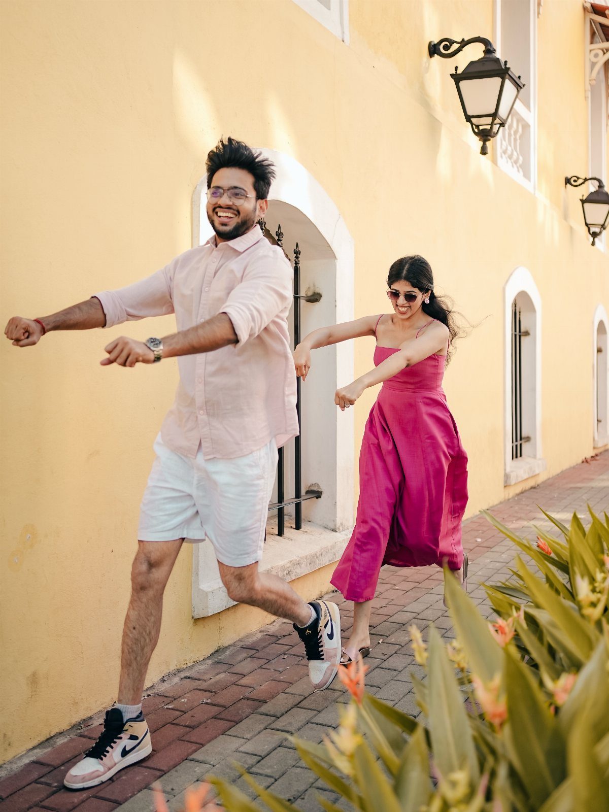 A joyful couple dancing and laughing on a sunny street by a yellow wall.