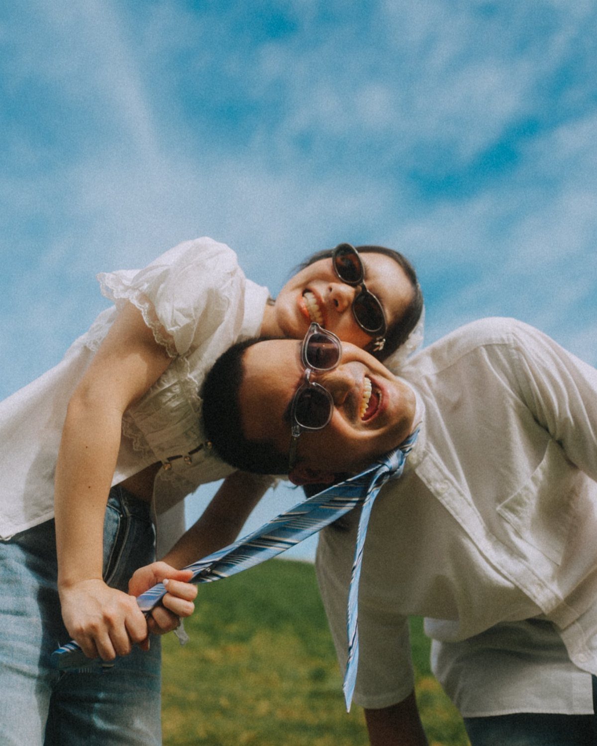 Couple in white shirts posing playfully with woman pulling man's blue striped tie.