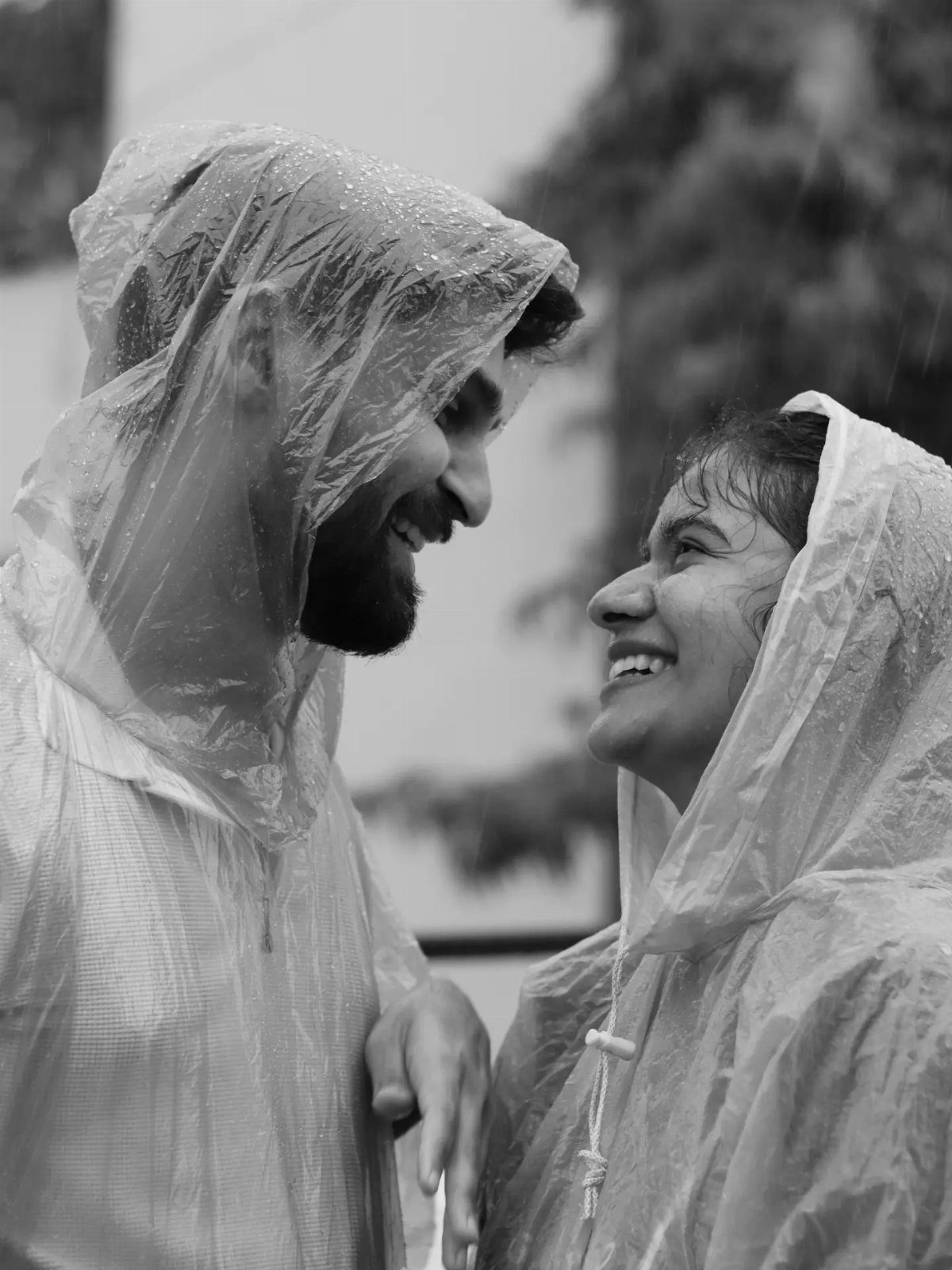 Smiling couple wearing plastic rain ponchos looking at each other in the rain