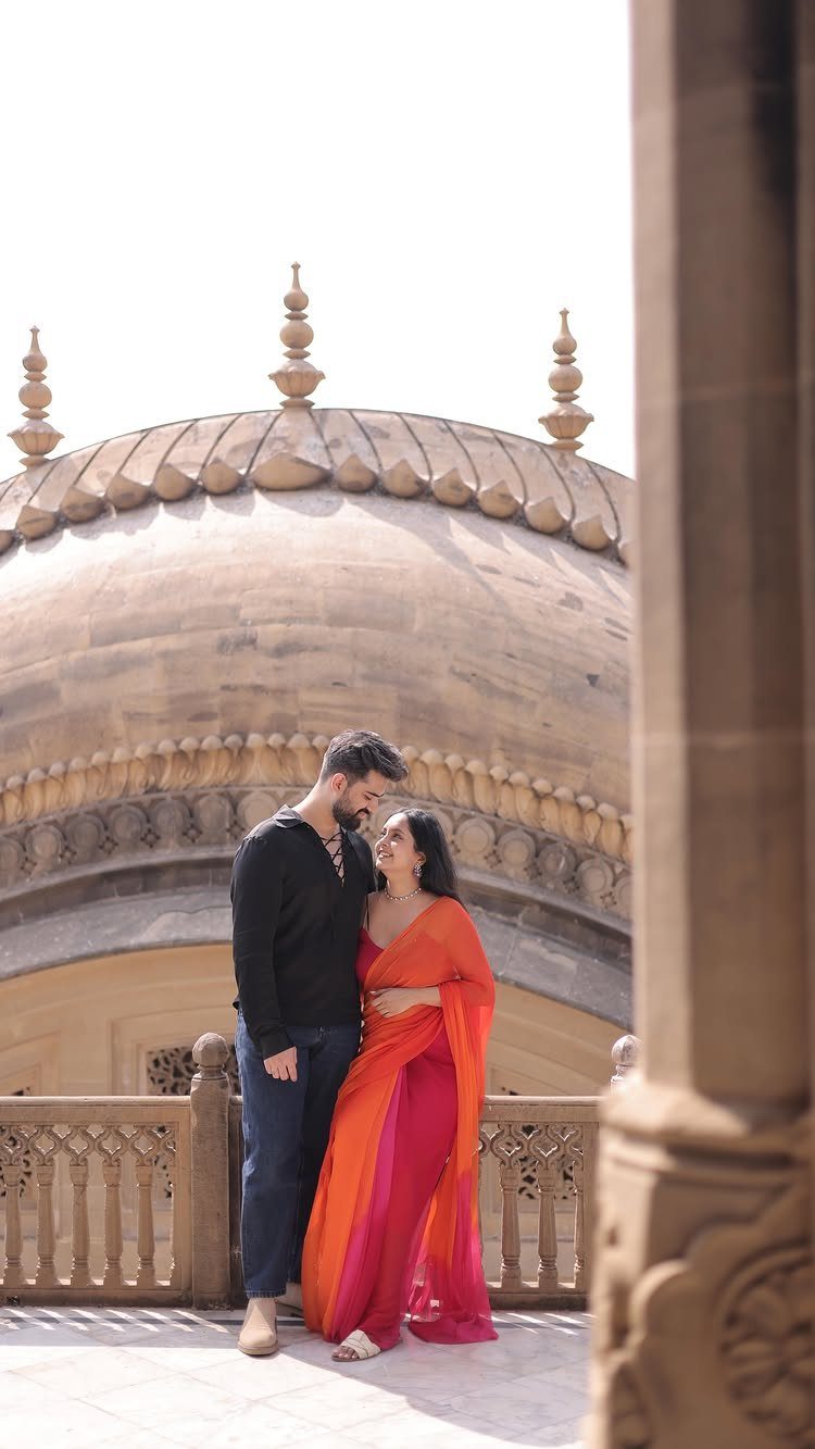 Couple posing in front of a grand sandstone palace dome in traditional attire.
