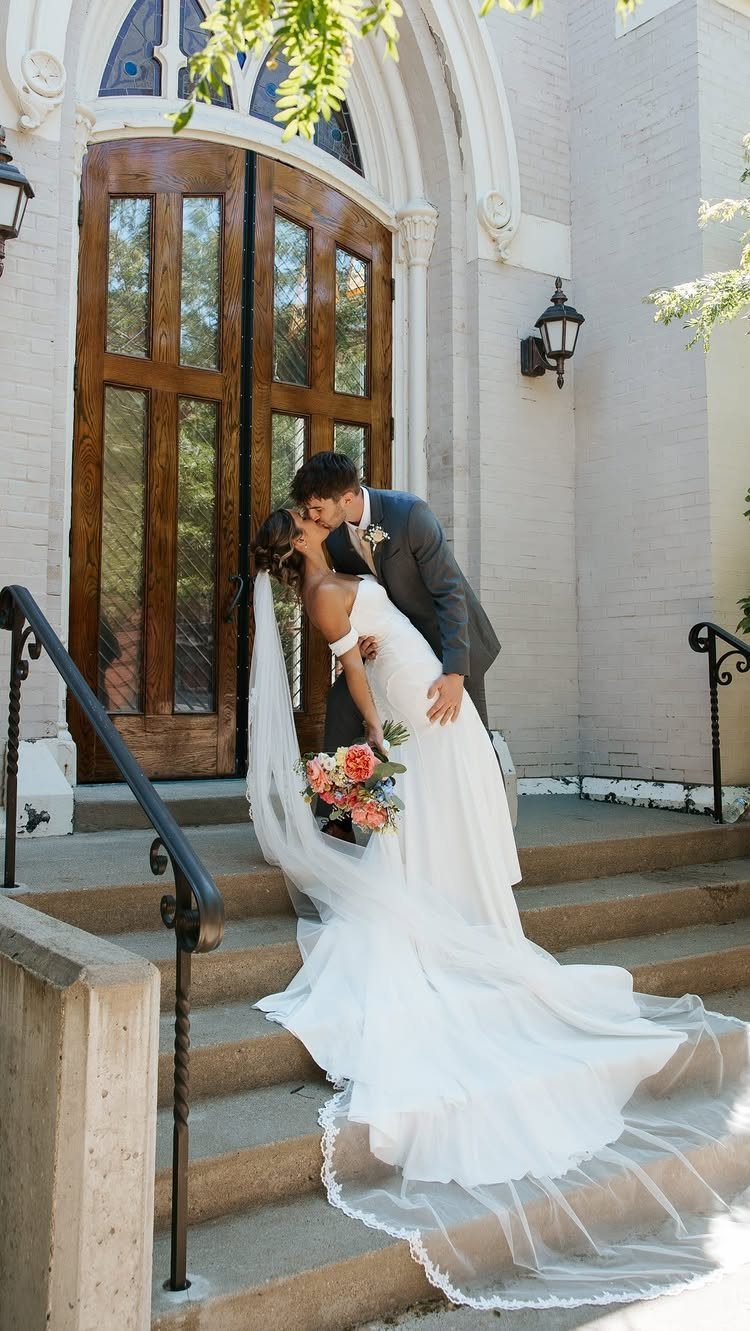 Bride and groom kissing on church steps in front of large wooden doors