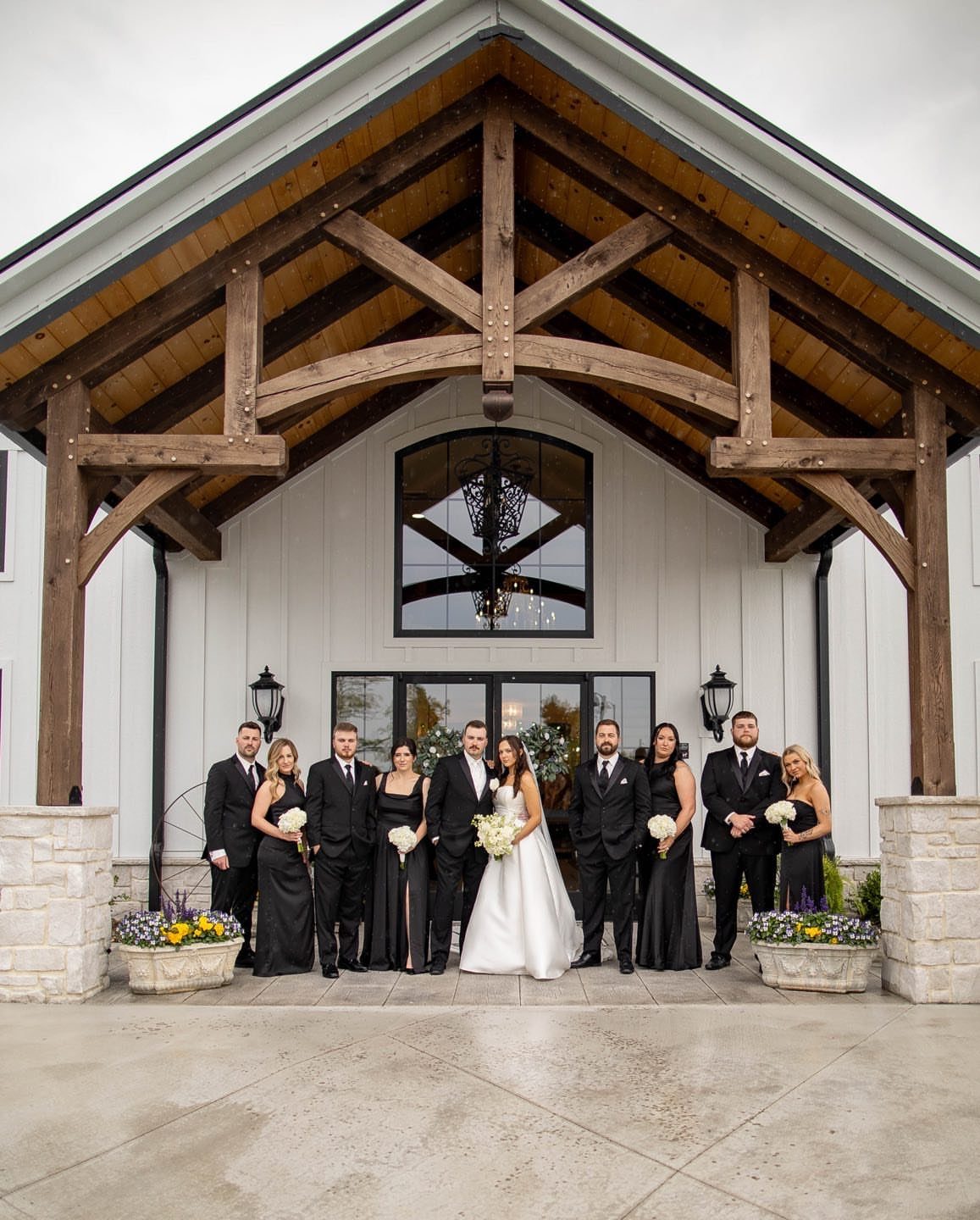 Wedding party posing under a rustic wooden porch in front of a white building