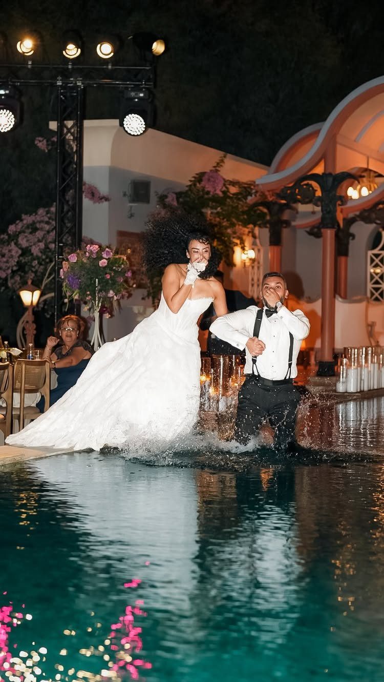 Bride and groom splashing in a swimming pool during a nighttime wedding celebration.