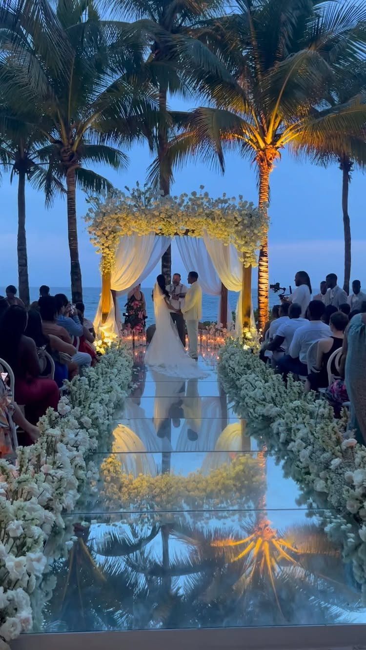 Wedding couple standing under a floral arch with a mirrored reflective aisle walkway
