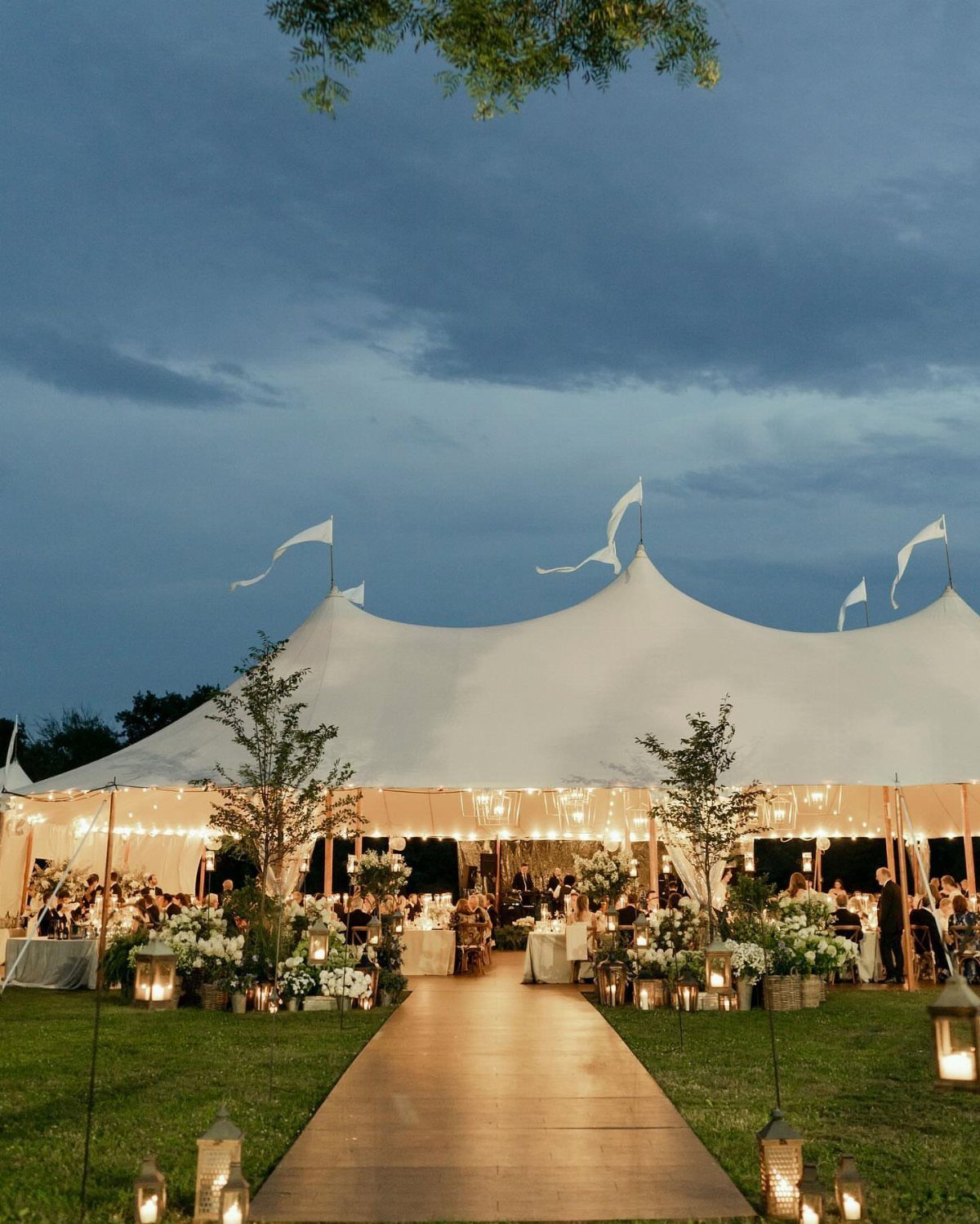 White wedding tent with string lights and floral arrangements on a grassy lawn