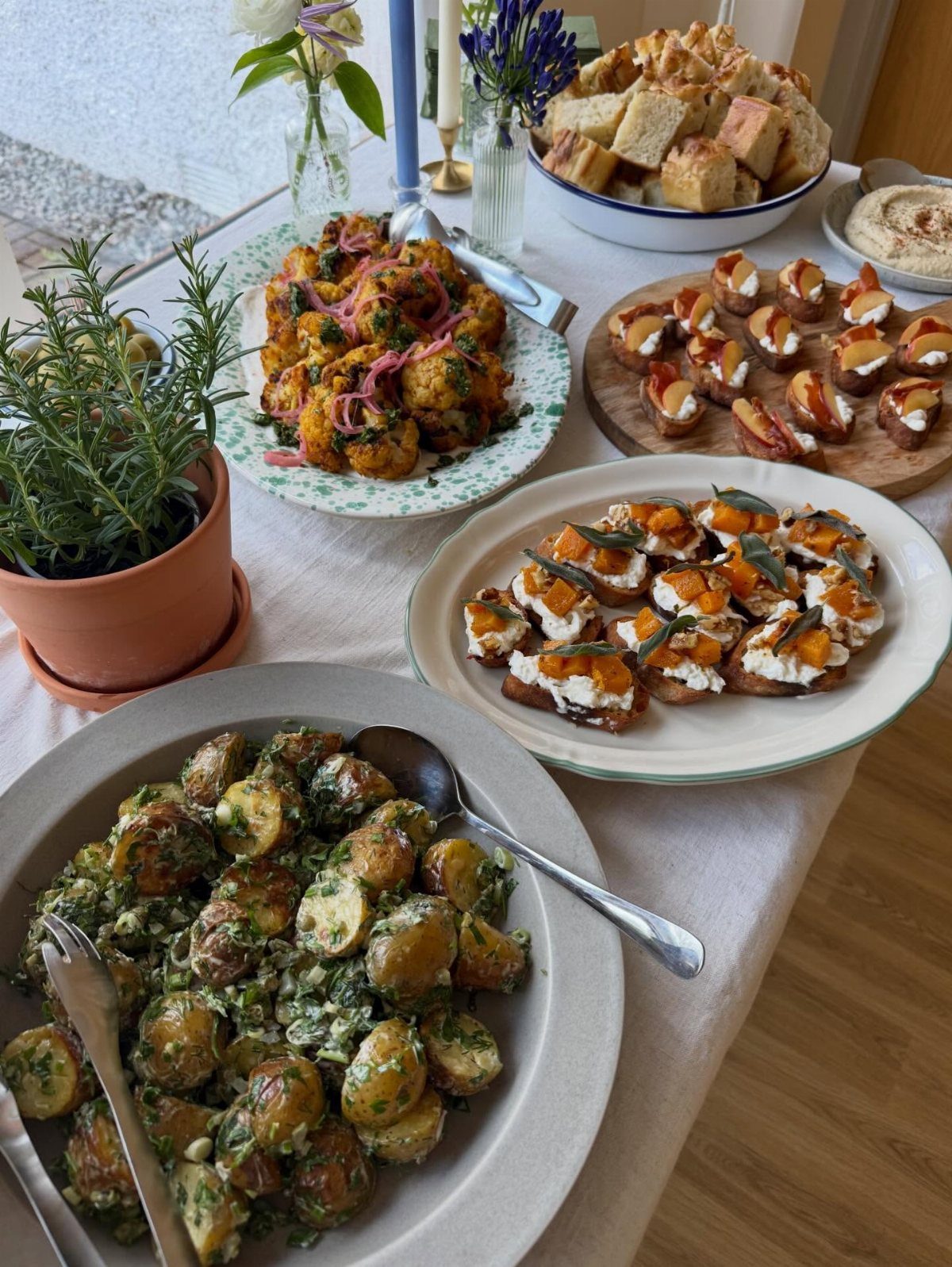 Assorted appetizer platters including potato salad and crostini on a white tablecloth.