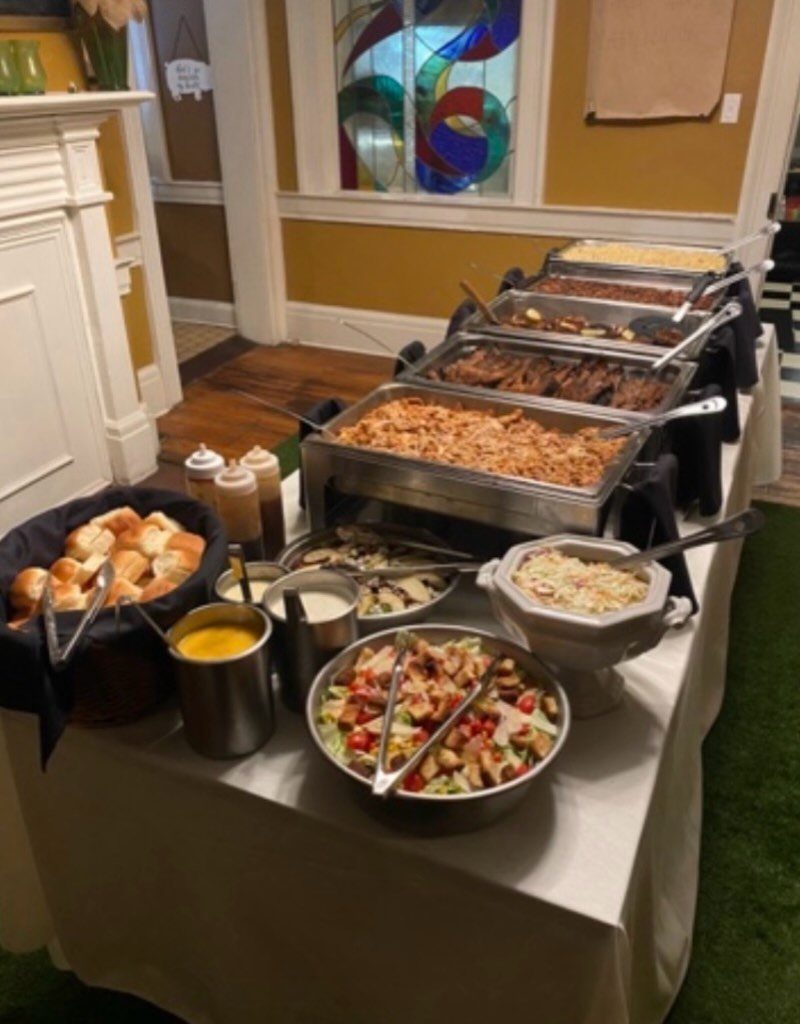 Buffet table with chafing dishes of grilled meats, salads, and rolls.