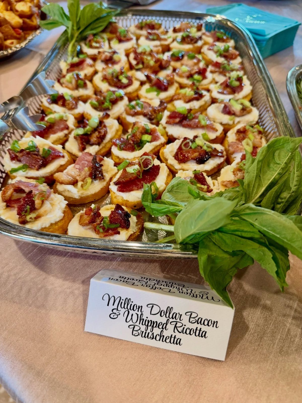 Bacon and whipped ricotta bruschetta on a silver platter with a name card.