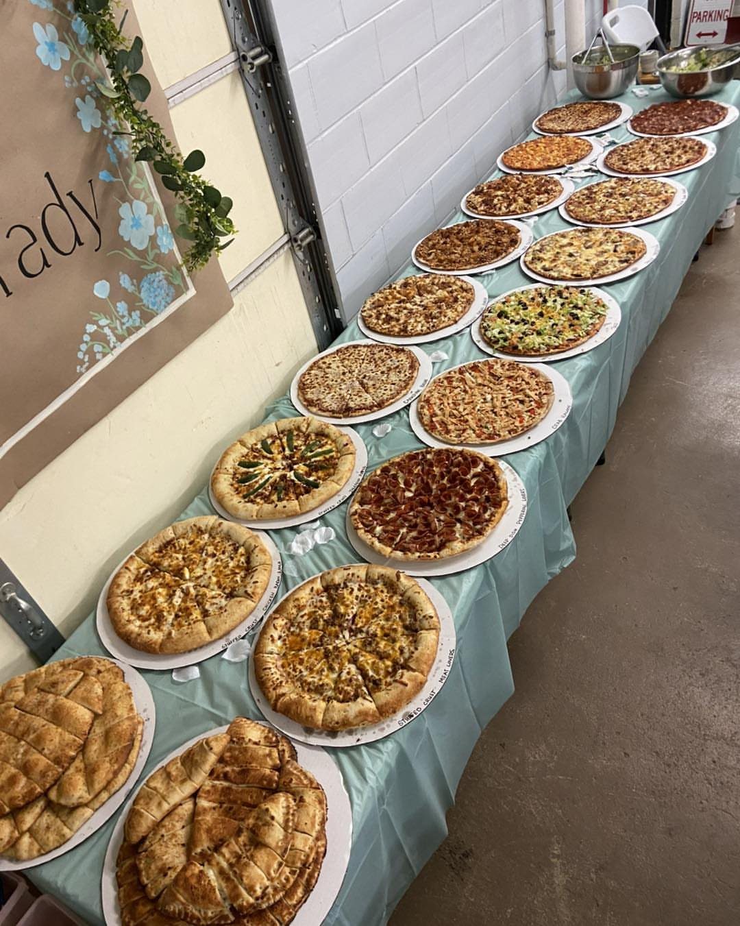 Various round pizzas with different toppings arranged on a light blue buffet table.