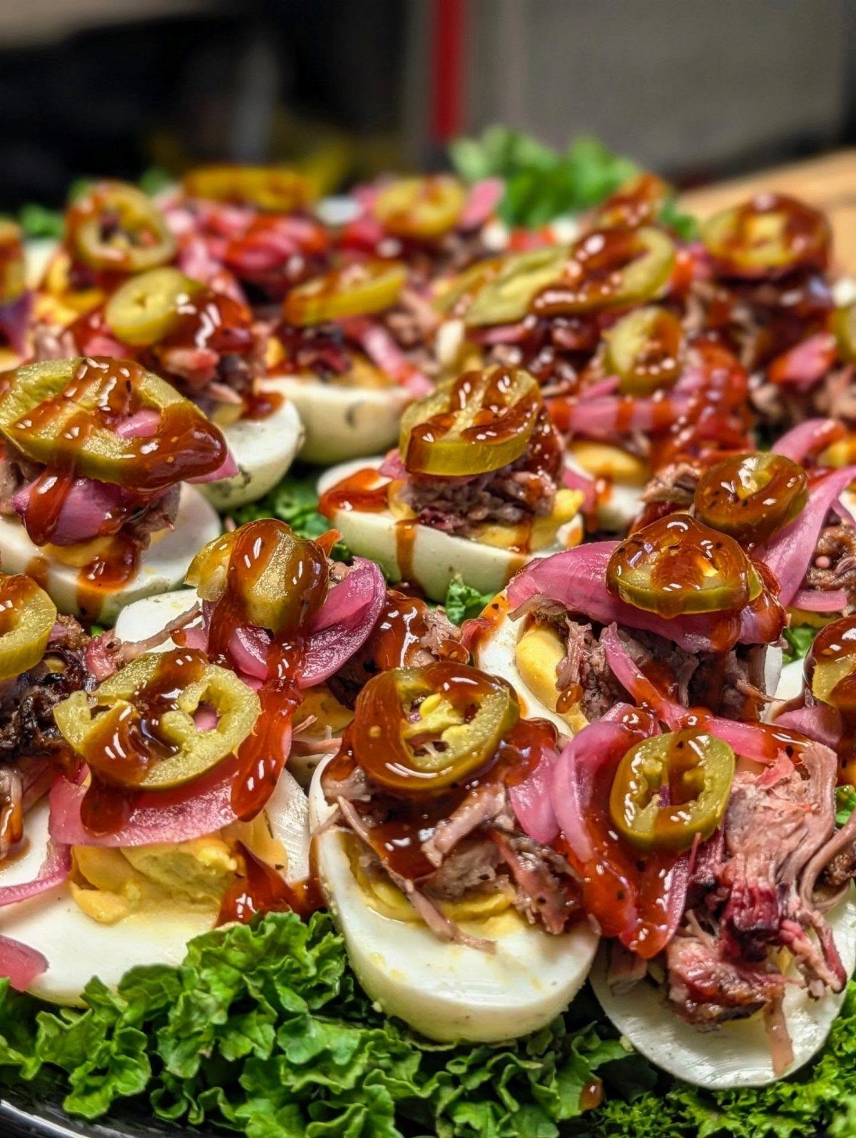 Deviled eggs topped with pulled pork, barbecue sauce, and jalapeños on green lettuce.