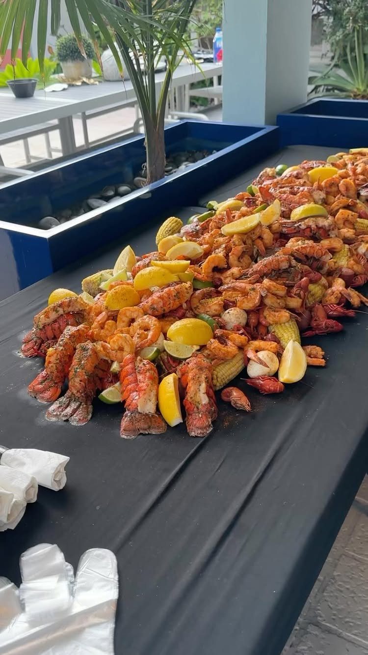 Seafood boil with lobster, shrimp, and corn on a black tablecloth outdoors.