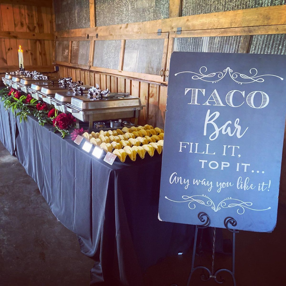 Taco bar buffet with silver chafing dishes, corn tortillas, and a chalkboard sign.