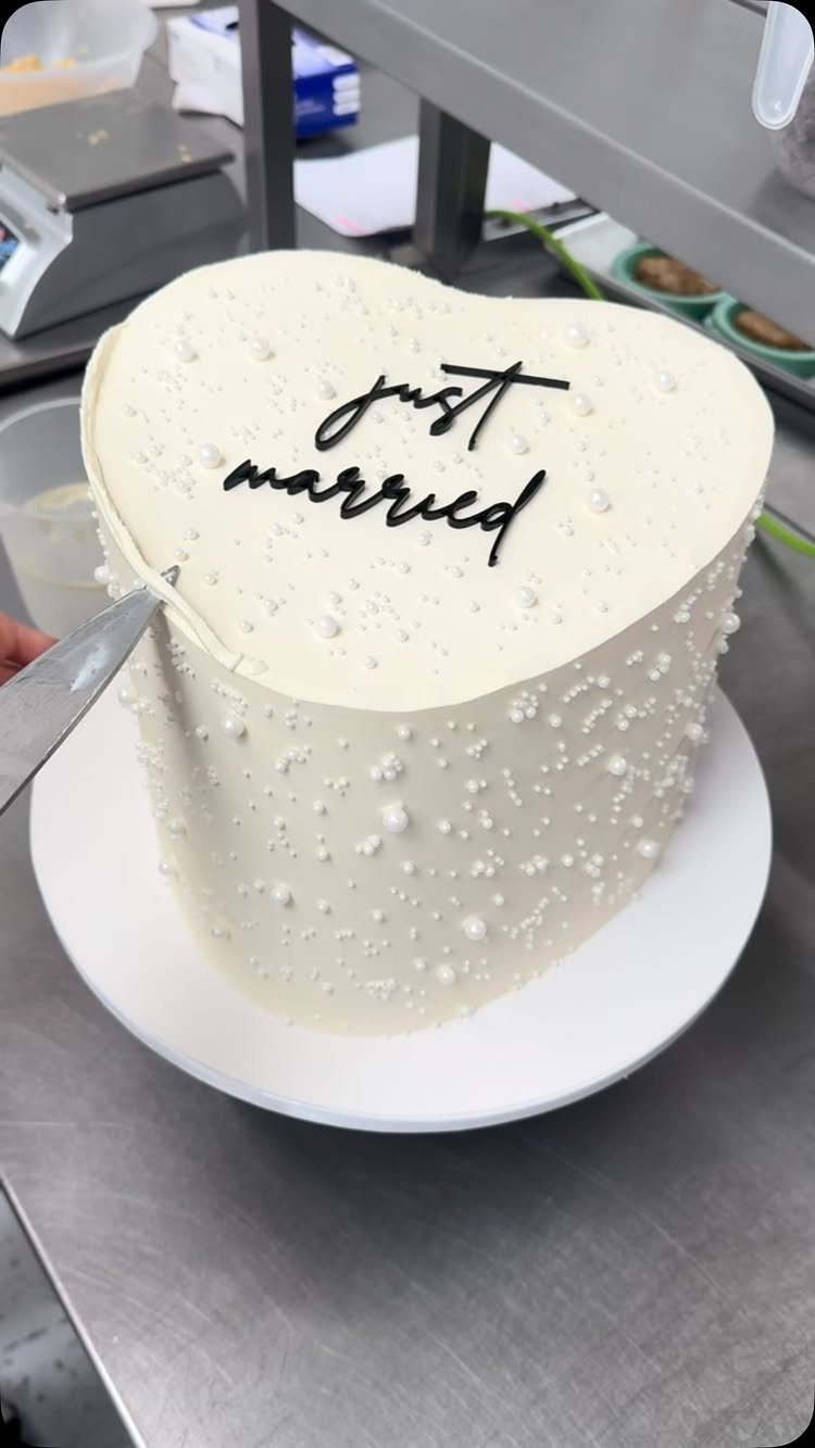 Heart-shaped white wedding cake with pearl frosting and just married text on top