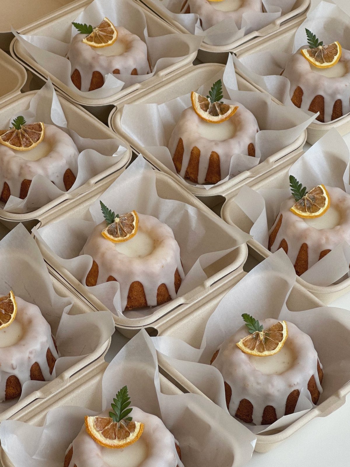 Mini bundt cakes with white glaze and dried lemon slices in cardboard containers.