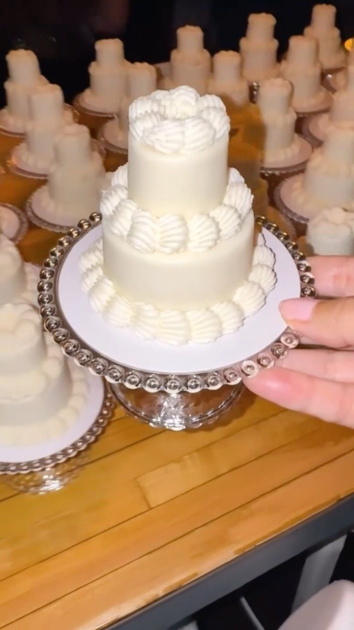 Small two-tier white wedding cake on a silver pedestal with others in background