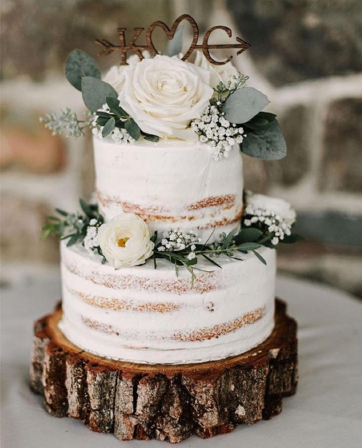 Two-tier naked wedding cake with white flowers on a rustic wood slice base