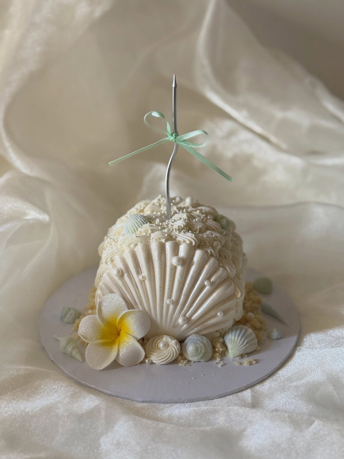 Seashell shaped mini cake decorated with edible shells and a plumeria flower