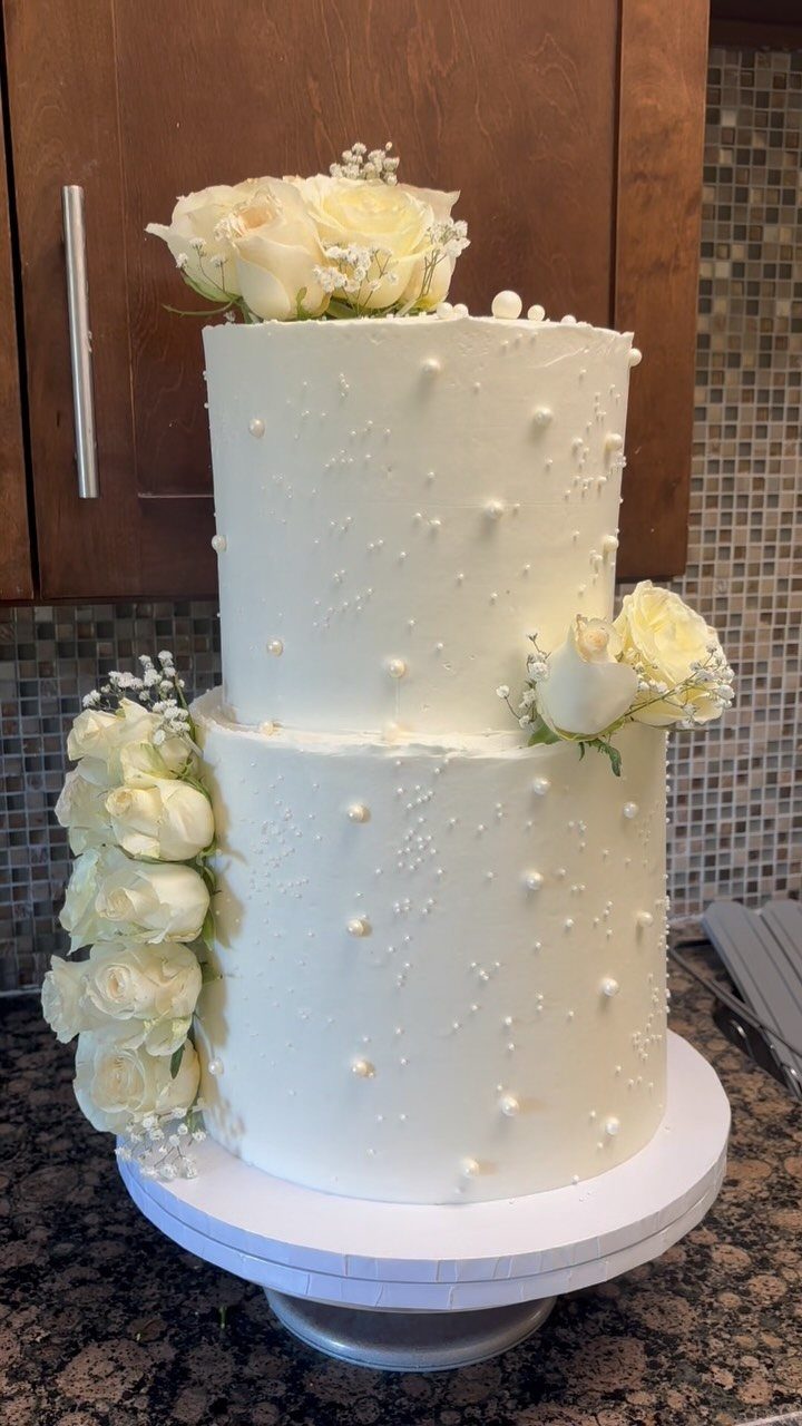 Two-tier white wedding cake decorated with edible pearls and fresh white roses.