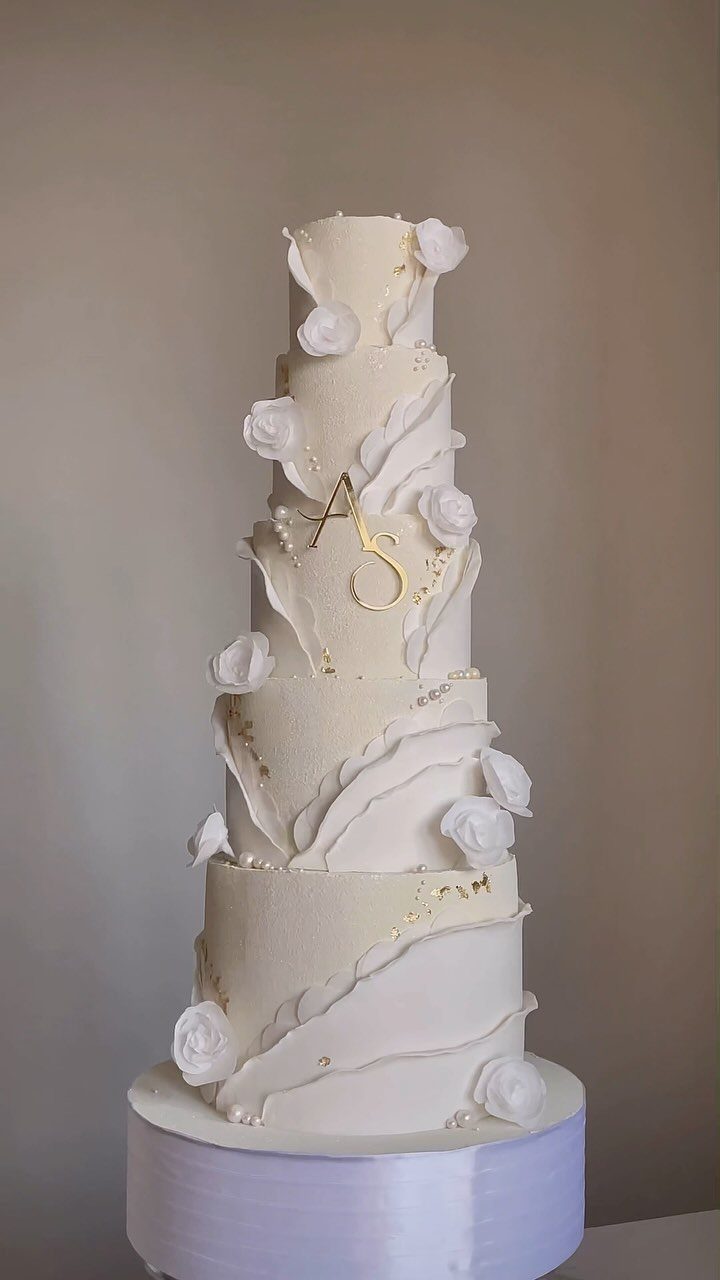 Multi-tiered white wedding cake with white roses and gold monogram on white stand