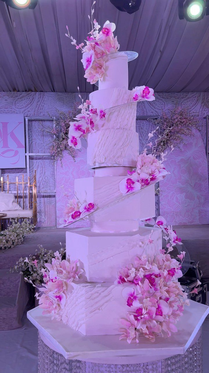Multi-tiered white wedding cake adorned with pink and white orchids on a pedestal.
