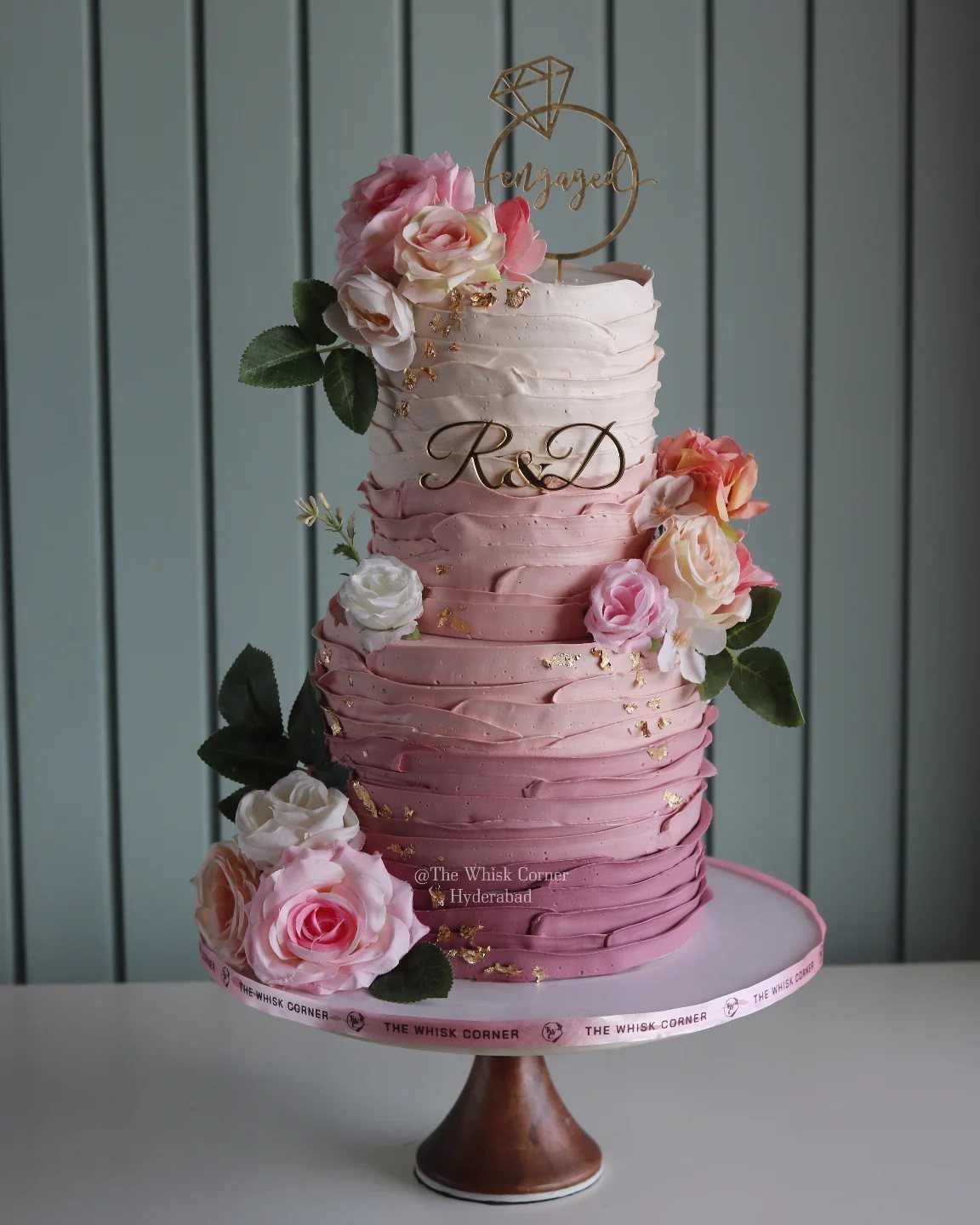 Two-tier pink ombre wedding cake decorated with fresh roses and gold accents.