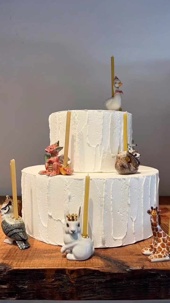 Two-tier white cake decorated with animal figurines holding yellow candles on wooden table